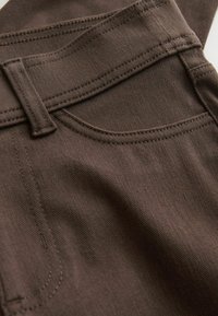 Prim-plan cu țesătură de denim maro, arătând un buzunar frontal, buclă pentru curea și cusături detaliate.