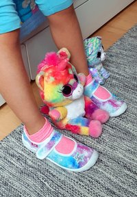 Kleurige schoenen met een sterrenstelselpatroon en roze accenten, gedragen met lichtroze sokken, naast pluchen unicorns. Textuur vloermat eronder.