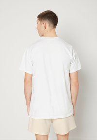 T-shirt en coton blanc à manches courtes, col rond et coupe décontractée, vue de dos, assortie à un short beige.