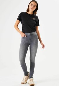 Zwart katoenen t-shirt met korte mouwen en een gouden graphic. Strakke grijze denim jeans met een soepele textuur. Lichte sneakers.