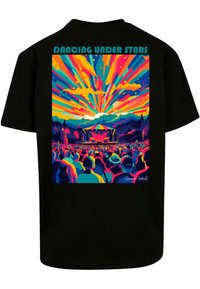 Camiseta negra con un gráfico vibrante que presenta rayos multicolores sobre un público de concierto y montañas, titulado "Bailando Bajo las Estrellas."