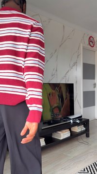 Pull rayé rouge et blanc, pantalon noir ; l'écran de télévision affiche du texte. Le mur présente un motif en marbre, avec une porte au design rayé.
