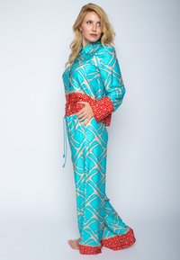 Gemustertes Loungewear-Set in Türkis mit einem beigen geometrischen Design. Mit einem roten Bund und Bündchen sowie einem spiraligen weißen Akzentmuster.