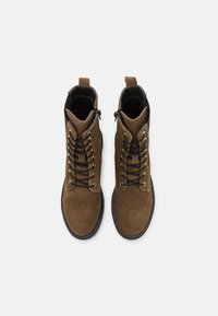 Botas de peito de camurça castanhas com realces pretos, apresentando ilhós dourados, frente com atacadores e zíperes laterais para um ajuste seguro e fácil de calçar.