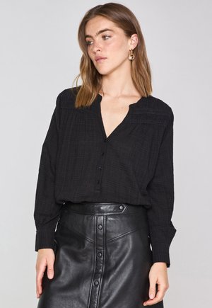 Black button-up shirt with long sleeves, textured fabric, and a V-neckline, paired with a high-waisted black leather skirt featuring snap buttons.