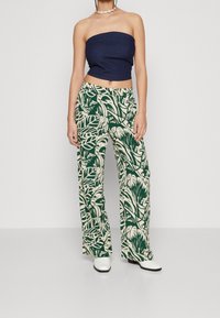 Džínová top bez ramínek v kombinaci s krémovými kalhotami širokého střihu s vzorem zelených listů; modelka má na sobě bílé kotníkové boty.