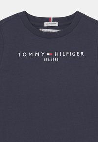 Navyblaue Bio-Baumwoll-T-Shirt mit weißem "TOMMY HILFIGER"-Logo und roten sowie weißen Akzenten, Rundhalsausschnitt, glatte Textur.