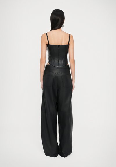 Melna ādas saīsināta bustier jakas ar plānām siksnām un rāvējslēdzēju aizmugurē, apvienota ar augsto jostasvietu platām biksēm, arī melnā ādā.