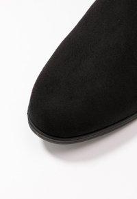 Bottine en suede noir avec un bout arrondi et une semelle en caoutchouc lisse. La texture est douce et mate, sans éléments métalliques ni motifs visibles.