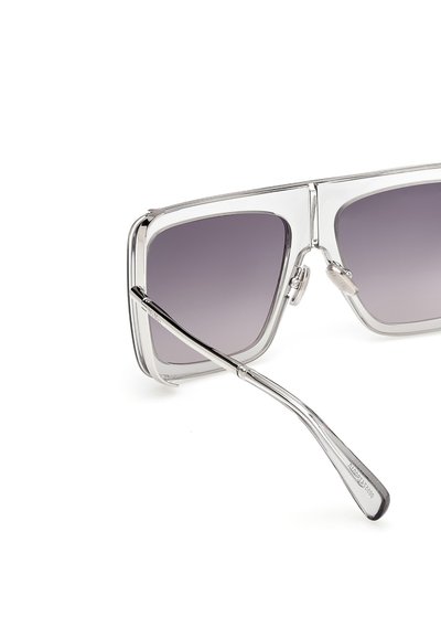 Un par de gafas de sol de gran tamaño con un marco transparente, lentes gris degradado y brazos metálicos delgados. Detalles de agarre texturizado en las almohadillas de la nariz.