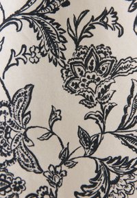 Motif de vigne noir floral et feuillu imprimé sur tissu beige avec un travail de ligne complexe et détaillé et des formes variées de pétales et de feuilles.