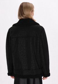 Schwarze Schaffelljacke mit einem weichen, strukturierten Kragen und Bündchen. Verfügt über eine taillierte Taille und ein glattes Leder-Finish. Rückansicht gezeigt.