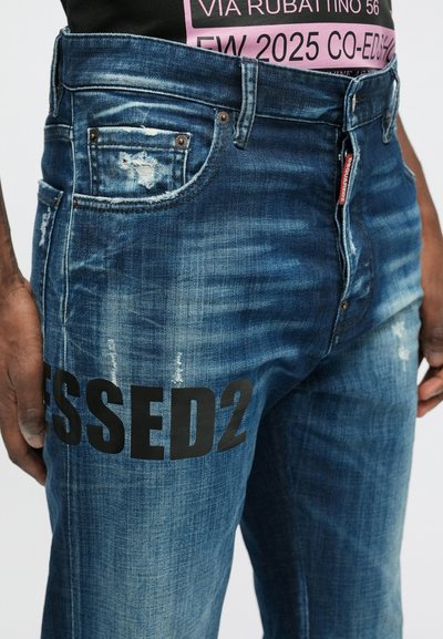 Modré deninové džínsy s vybledlým vzhľadom, na boku s čiernou grafikou "SSED2". Obsahujú klasický dizajn s piatimi vreckami a kovovými detailmi.