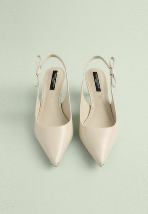 Beige kengät, joissa on terävä pää ja nilkkasiteet, näyttävät sileältä ja niissä on kaunis bow-yksityiskohta kantapäässä. Muotoilu on yksinkertainen ja minimalistinen.