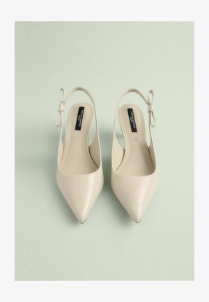 Beige színű, hegyes orrú, hátul nyitott cipők sima textúrával, masni díszítéssel a sarkon és elegáns, minimális dizájnnal.