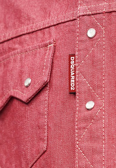 Détail d'une chemise en denim rouge avec une poche munie d'un bouton-pression argenté et des coutures blanches, étiquetée avec une marque DSQUARED2.