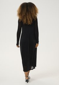 Black, long-sleeve dress with a pleated waist and a sheer overlay, featuring a silky texture and subtle shimmer. Worn with silver heels.