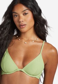 Top bikini verde a coste con coppe triangolari e sottili spalline regolabili. Una collana dorata con piccoli accenti bianchi è indossata attorno al collo.