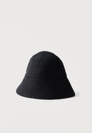 Sombrero tipo pescador de crochet negro con patrón de punto texturizado y ala suavemente acampanada sobre un fondo claro liso.