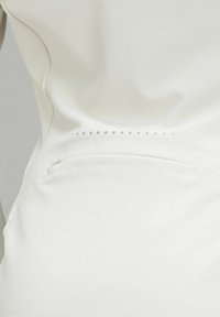 Rochie din țesătură albă, cu o textură fină, având o serie decorativă de mici perforații pe spate și un detaliu de buzunar discret pe lateral.