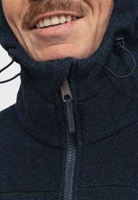 Dunkelblaues Fleece-Jackett mit hohem Kragen, Reißverschluss und verstellbarem Kapuzenkragen, das ein strukturiertes Strickmuster und Zugkordeln aufweist.