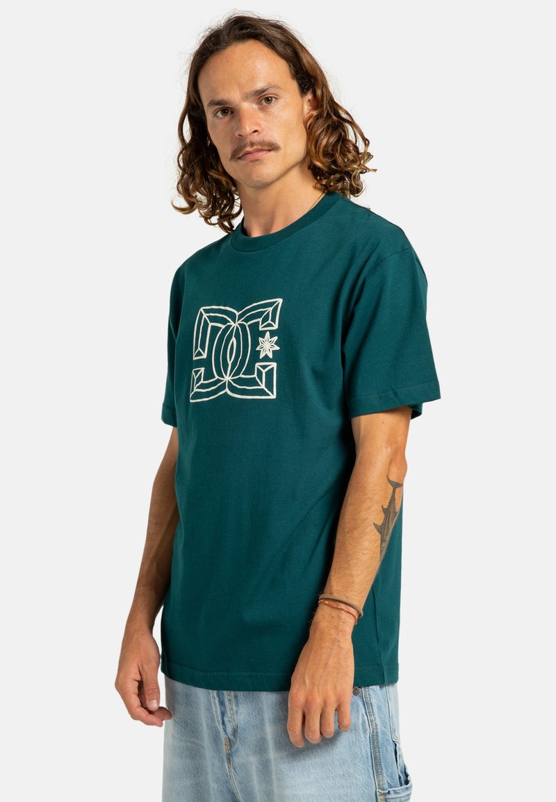 Camiseta de algodón color teal con cuello redondo, que presenta un diseño gráfico blanco en el centro. Manga corta y ajuste relajado.
