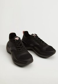 Black athletic shoes with a mesh upper, featuring textured panels, a rounded sole, and pink accents on the heel and tongue.