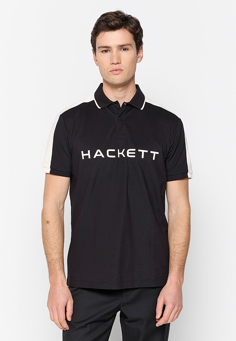 Schwarzes Poloshirt mit weißen Akzenten an den Schultern, mit einem großen "HACKETT"-Logo in Weiß auf der Vorderseite. Kurze Ärmel und klassischer Kragen.