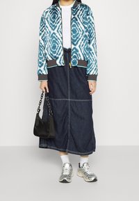 Modrá a bílá vzorovaná bomber bunda přes bílé tričko, doplněná dlouhou džínovou sukní, stříbrnými teniskami a černou kabelkou.