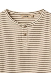 Približan posnetek bež in bele majice z rebrastim vzorcem za otroke, okroglim izrezom in dvema rjavima gumboma pod ovratnikom.