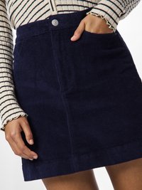 Σκούρα μπλε κοτλέ φούστα με μπροστινή κουμπί και πλαϊνές τσέπες. Το ύφασμα έχει ραβδωτή υφή και το τελείωμα είναι ευθύ.