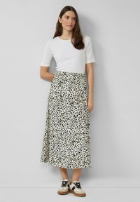 Witte, getailleerde top gecombineerd met een middellange, crèmekleurige rok met een zwart stippenpatroon. Model draagt zwart-witte sneakers.