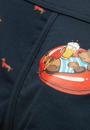 Cartoon dachshund wearing a blue striped shirt, lying on a red float holding a beer mug, with smaller dachshund patterns on dark fabric.