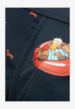 Cartoon teckel die een blauw gestreept shirt draagt, liggend op een rode drijfmat en een bierpul vasthoudt, met kleinere teckelpatronen op donkere stof.