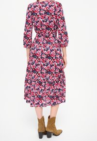 Vestido floral de largo medio con cintura fruncida, con un fondo azul marino y un patrón de flores en rosa, rojo y azul. Combinado con botines de ante en color beige.