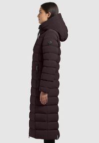 Long, dark brown puffer coat with a hood. Features quilted design, two side zippers, and a logo patch on the left arm.