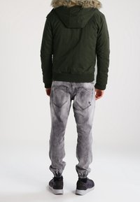 Grøn bomberjakke med kunstpels hætte, parret med lysegrå, tapered jeans med elastiske manchetter og sorte sneakers.