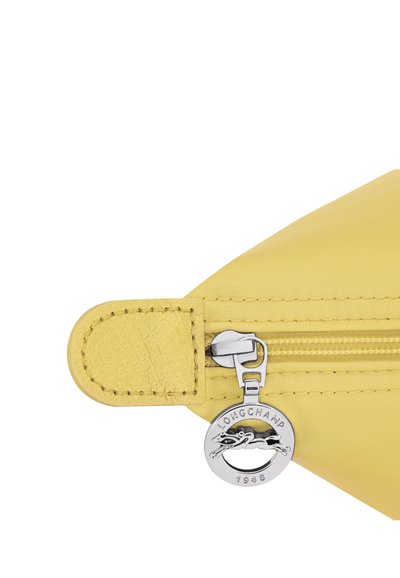 Yellow fabric pouch corner with yellow leather tab and silver circular zipper pull engraved "LONGCHAMP 1948" with a horse logo.