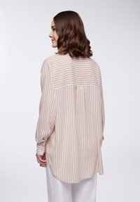 Camicia a righe beige e bianche con bottoni, maniche lunghe, tessuto morbido, orlo curvo e dettaglio della cucitura sulla schiena.
