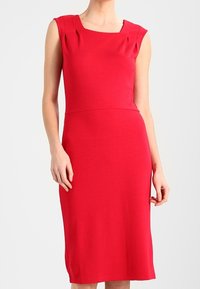 Robe sans manches rouge avec un décolleté carré, une coupe ajustée et des plis verticaux aux épaules. Fabriquée en tissu lisse et extensible.