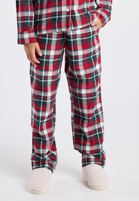 Rood en groene geruite pyjama-set met een knoopsluiting aan de bovenkant en bijpassende broek. Zacht materiaal met een losse pasvorm en witte fluffy slippers.