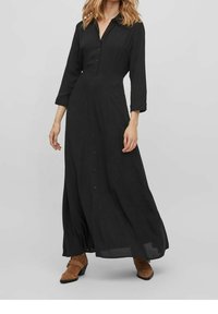 Černé dlouhé šaty s dlouhým rukávem a zapínáním na knoflíky vpředu, s volným střihem, vyrobené z měkké tkaniny. Mají límec.