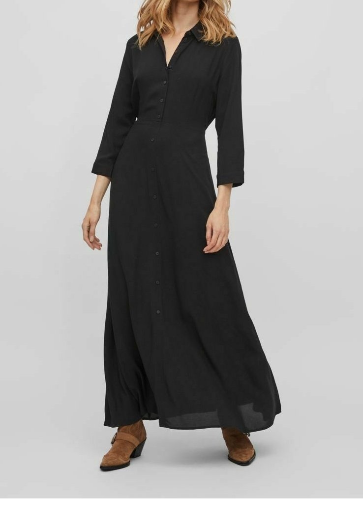 Černé dlouhé šaty s dlouhým rukávem a zapínáním na knoflíky vpředu, s volným střihem, vyrobené z měkké tkaniny. Mají límec.