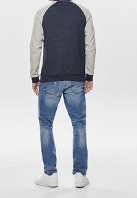 Granatowo-szara bluza raglanowa z teksturowanymi rękawami, w połączeniu z jasnoniebieskimi dżinsami i białymi trampkami, widok od tyłu.