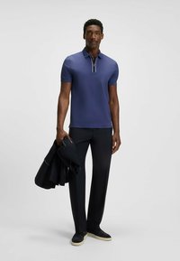 Granatowa koszulka polo z krótkim rękawem i zapięciem na zamek, z kontrastowym paskiem. Połączona z ciemnymi spodniami i marynarką.