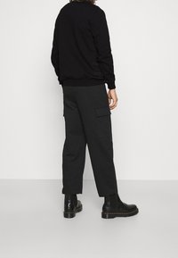 Maglione nero con polsini a coste, abbinato a pantaloni cargo scuri con tasche laterali. Stivaletti neri con suola spessa completano il look.