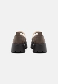 Bruine leren schoenen met dikke zwarte rubberen zolen. Voorzien van een zachte, beige bontvoering langs de bovenrand en een trekband aan de achterkant.