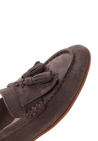 Bruine suède loafer met kwastjes, gedetailleerd stiksel en een gladde, lichtbruine zool, diagonaal geplaatst tegen een witte achtergrond.