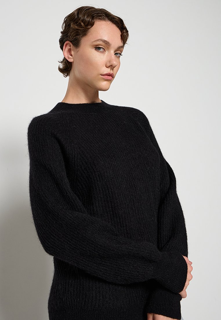 Schwarzer, gestrickter Pullover mit gerippter Textur, rundem Ausschnitt und voluminösen Ärmeln. Hergestellt aus einem weichen, flauschigen Garn.