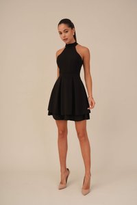 Abito nero con scollo a halter, dal corpetto aderente e gonna svasata. Realizzato in tessuto liscio, con pieghe e orlo a strati. Indossato con tacchi nudi.